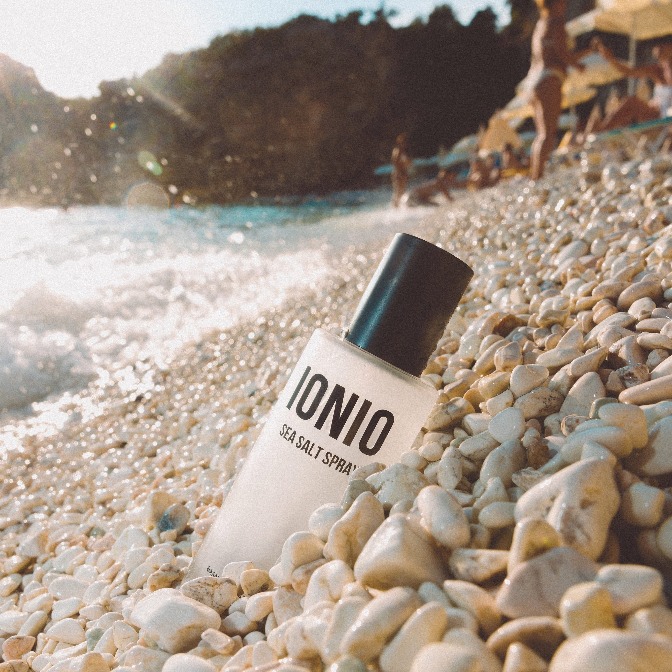 IONIO hair salt spray bottle on a pebbly beach with a scenic background