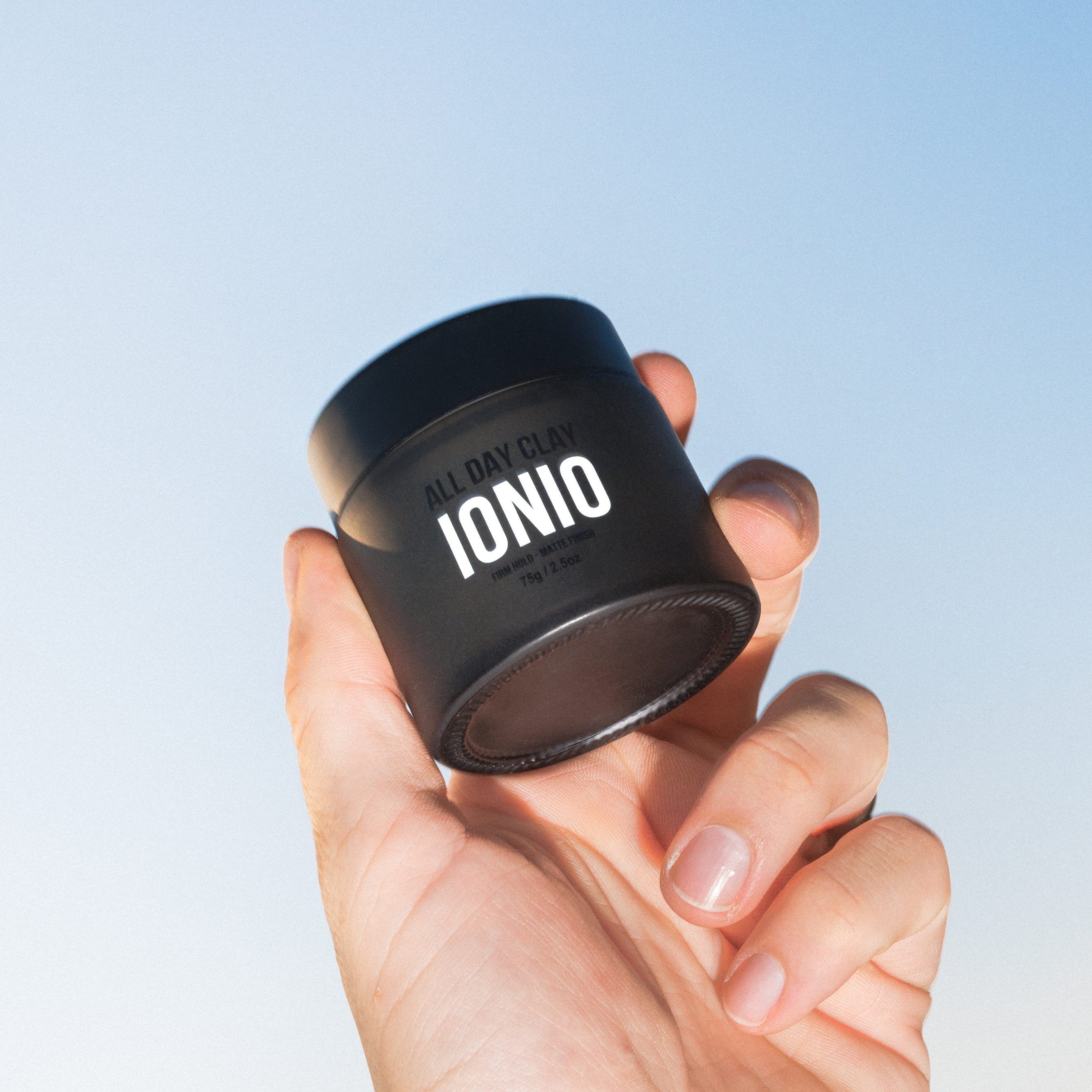 Hand holding a black container labeled 'IONIO' against a light blue background