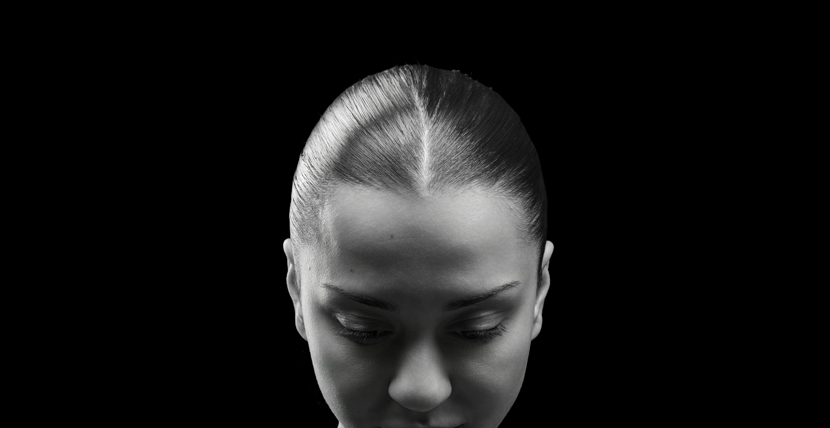 Black and white portrait of a woman with a neutral expression on a black background